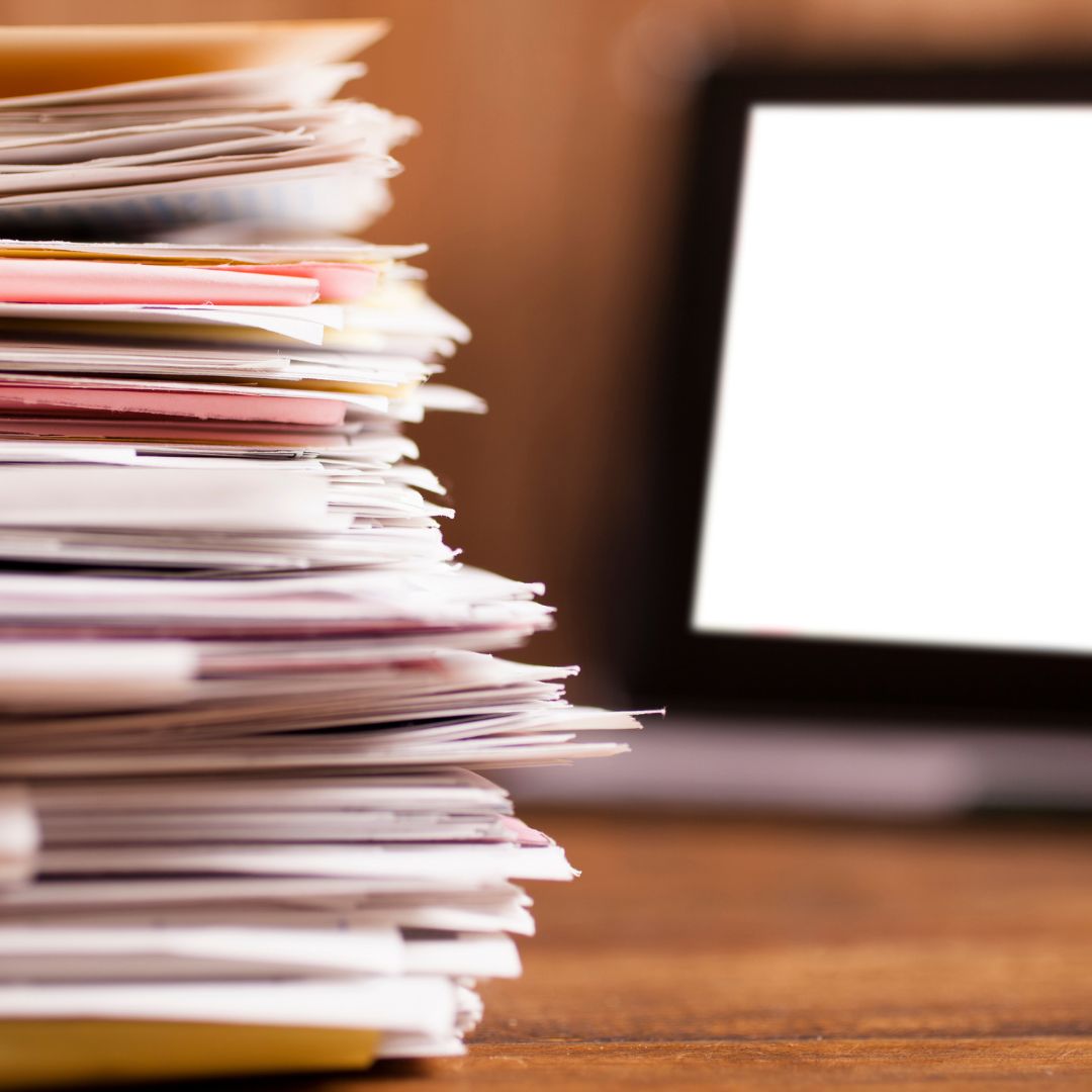 stack of paperwork in front of a computer